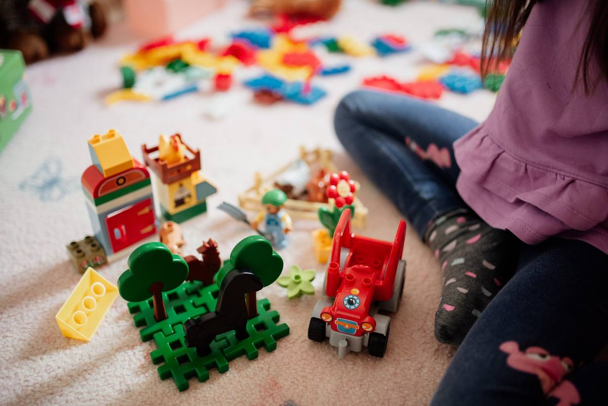 Kind spielt auf dem Boden mit bunten Bausteinen, Figuren und einem Spielzeugauto