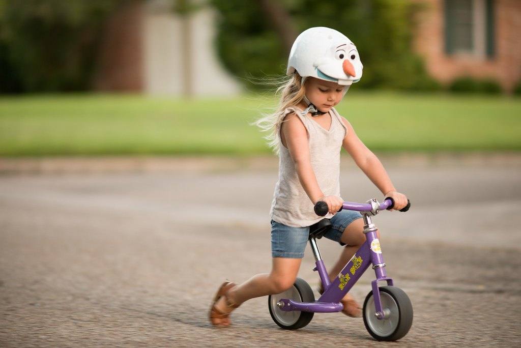 Mädchen mit Helm fährt auf einem Laufrad die Straße entlang