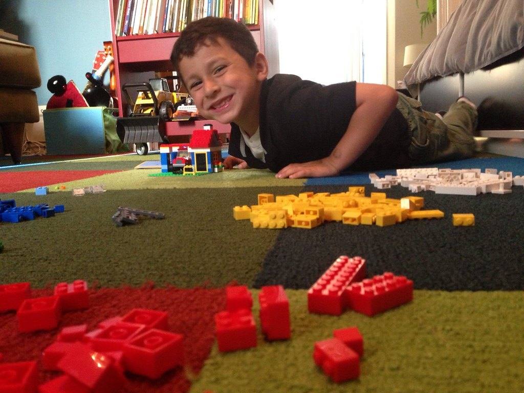 Junge liegt zwischen LEGO-Steinen auf dem Boden