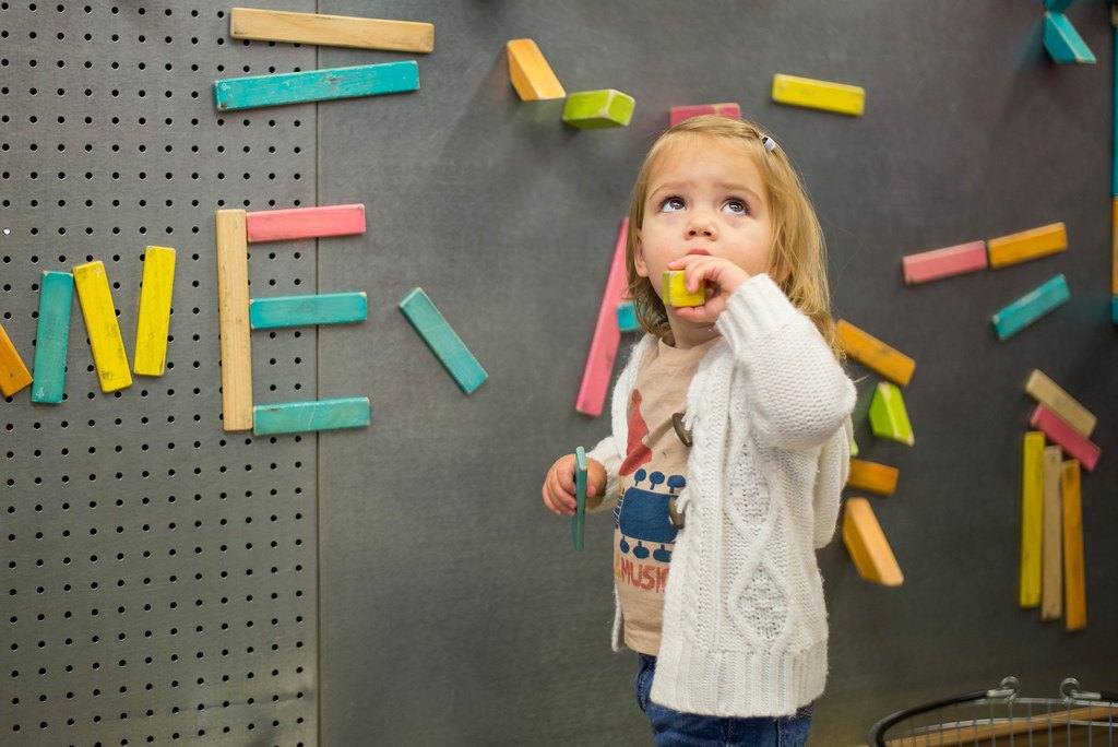 Mädchen spielt mit magnetischen Holzstäben an einer Wand